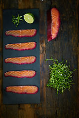 Image showing Sliced salmon fillet, salted with beetroot juice, served on whole wheat with salad leaves, sea salt and pepper over metal surface. Top view