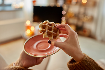 Image showing hands of young woman eating waffle at home