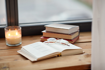 Image showing books, glasses and candle burning on window sill