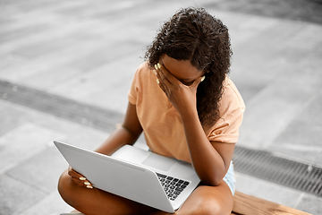 Image showing stressed african student girl with laptop in city