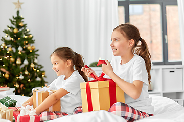 Image showing happy sisters with christmas gifts in bed at home