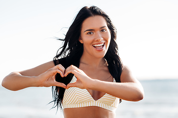 Image showing smiling young woman in showing hand heart on beach