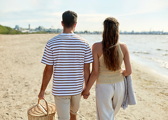 Image showing happy couple with picnic basket walking on beach