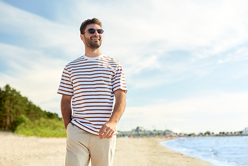 Image showing young man in sunglasses walking along summer beach