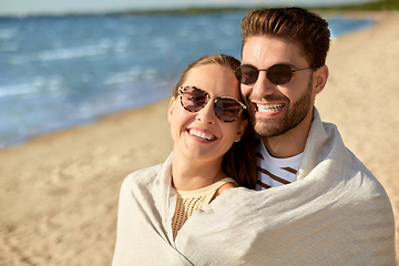 Image showing happy couple covered with blanket hugging on beach