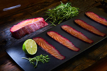 Image showing Sliced salmon fillet, salted with beetroot juice, served on whole wheat with salad leaves, sea salt and pepper over metal surface. Top view