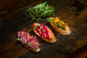 Image showing Assorted bruschetta with roast beef, vegetables and lightly salted salmon with greens leaves on wooden background.