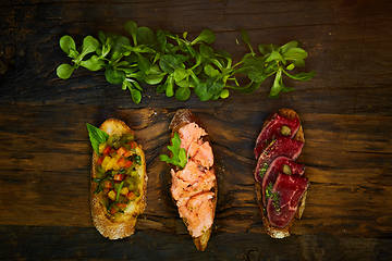 Image showing Assorted bruschetta with roast beef, vegetables and lightly salted salmon with greens leaves on wooden background.