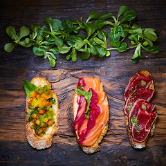 Image showing Assorted bruschetta with roast beef, vegetables and lightly salted salmon with greens leaves on wooden background.