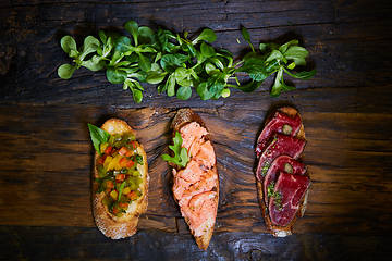 Image showing Assorted bruschetta with roast beef, vegetables and lightly salted salmon with greens leaves on wooden background.