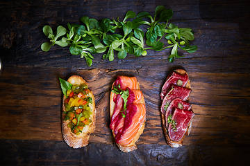 Image showing Assorted bruschetta with roast beef, vegetables and lightly salted salmon with greens leaves on wooden background.