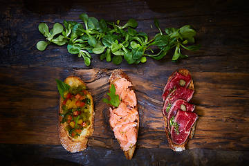 Image showing Assorted bruschetta with roast beef, vegetables and lightly salted salmon with greens leaves on wooden background.