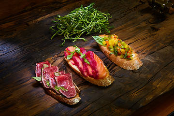 Image showing Assorted bruschetta with roast beef, vegetables and lightly salted salmon with greens leaves on wooden background.