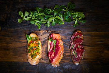 Image showing Assorted bruschetta with roast beef, vegetables and lightly salted salmon with greens leaves on wooden background.