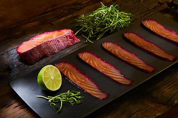 Image showing Sliced salmon fillet, salted with beetroot juice, served on whole wheat with salad leaves, sea salt and pepper over metal surface. Top view