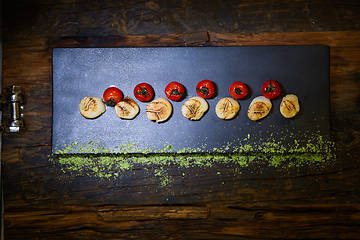 Image showing Fried scallops with tomatoes on a black plate. Shallow dof.