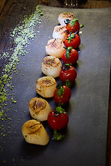 Image showing Fried scallops with tomatoes on a black plate. Shallow dof.