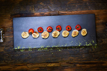 Image showing Fried scallops with tomatoes on a black plate. Shallow dof.