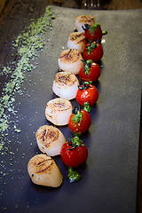 Image showing Fried scallops with tomatoes on a black plate. Shallow dof.