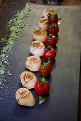 Image showing Fried scallops with tomatoes on a black plate. Shallow dof.