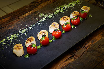 Image showing Fried scallops with tomatoes on a black plate. Shallow dof.