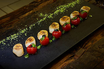 Image showing Fried scallops with tomatoes on a black plate. Shallow dof.