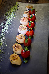 Image showing Fried scallops with tomatoes on a black plate. Shallow dof.