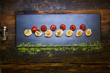 Image showing Fried scallops with tomatoes on a black plate. Shallow dof.