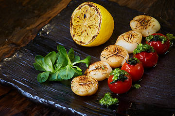 Image showing Fried scallops with tomatoes on a black plate. Shallow dof.