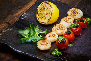 Image showing Fried scallops with tomatoes on a black plate. Shallow dof.