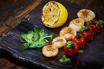 Image showing Fried scallops with tomatoes on a black plate. Shallow dof.