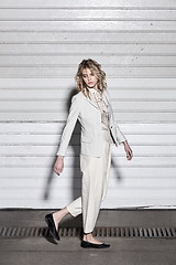 Image showing Full length fashion portrait of a woman standing against a wall on street. Street style