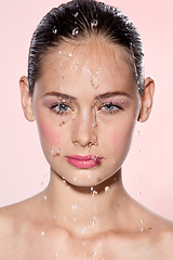 Image showing Beautiful Model Girl with splashes of water on her face. Beautiful Woman under splash of water with fresh skin over pink background. Skin care Cleansing and moisturizing concept. Beauty face