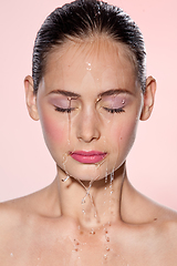 Image showing Beautiful Model Girl with splashes of water on her face. Beautiful Woman under splash of water with fresh skin over pink background. Skin care Cleansing and moisturizing concept. Beauty face