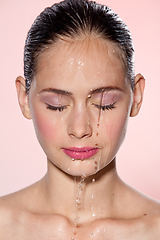 Image showing Beautiful Model Girl with splashes of water on her face. Beautiful Woman under splash of water with fresh skin over pink background. Skin care Cleansing and moisturizing concept. Beauty face