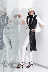 Image showing Beautiful young woman in white hat, high heels and white suit is standing, looking in camera. Full length studio shot on white background.