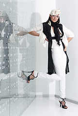 Image showing Beautiful young woman in white hat, high heels and white suit is standing, looking in camera. Full length studio shot on white background.