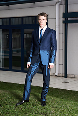 Image showing Portrait of an attractive young businessman in urban background wearing blue suit and necktie. Looking to the camera. Classic style.