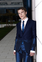 Image showing Portrait of an attractive young businessman in urban background wearing blue suit and necktie. Looking to the camera. Classic style.