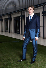 Image showing Portrait of an attractive young businessman in urban background wearing blue suit and necktie. Looking to the camera. Classic style.