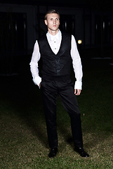 Image showing Male fashion, beauty concept. Portrait of young man with short wet hair wearing black suit, posing on street. Classic style.