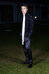 Image showing Male fashion, beauty concept. Portrait of young man with short wet hair wearing black suit, posing on street. Classic style.