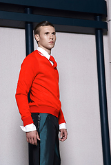 Image showing Portrait of an attractive young businessman in urban background wearing red jacket and red tie. Looking to the camera. Classic style