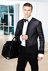Image showing Male fashion, beauty concept. Elegant young fashion man holds in his hand a black bag and looking to the camera. Classic style. Studio shot