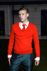 Image showing Portrait of an attractive young businessman in urban background wearing red jacket and red tie. Looking to the camera. Classic style