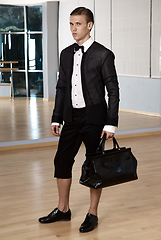 Image showing Male fashion, beauty concept. Elegant young fashion man holds in his hand a black bag and looking to away from the camera. Classic style. Studio shot