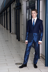 Image showing Portrait of an attractive young businessman in urban background wearing blue suit and necktie. Looking to the camera. Classic style.