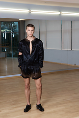 Image showing Man in elegant suite posing in fitness gym. High fashion young sexy man in black shorts and a black jacket