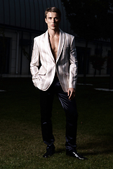 Image showing Elegant man in white jacket and black pants posing on green grass.