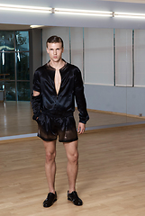 Image showing Man in elegant suite posing in fitness gym. High fashion young sexy man in black shorts and a black jacket